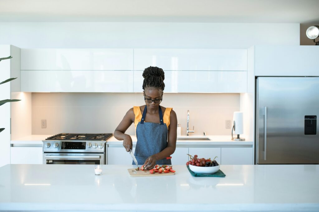 An adult woman in a modern kitchen slicing strawberries on a cutting board with a knife.